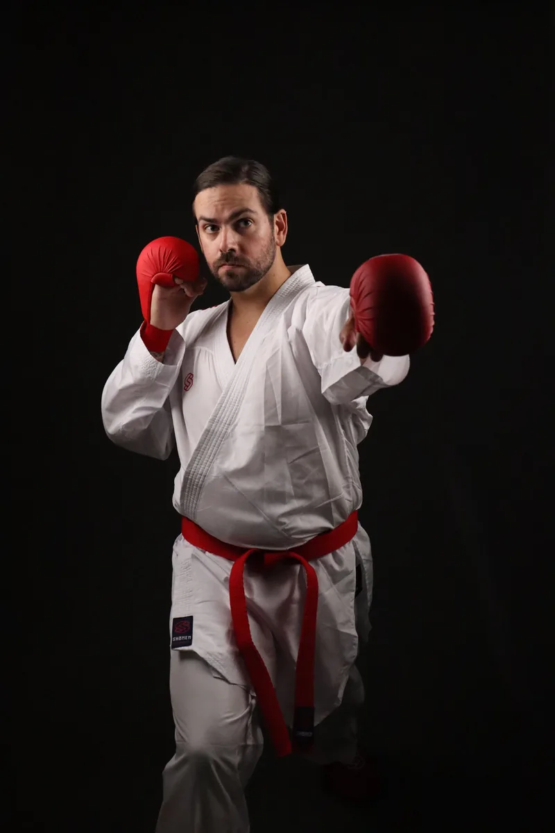 Atleta em posição de guarda com o kimono de kumite Shomen e luvas vermelhas